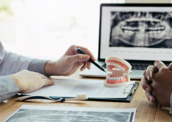 Dentist and patient discussing treatment plan at desk with X-ray and model teeth