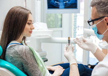 Dentist showing sample implant to patient in dental chair
