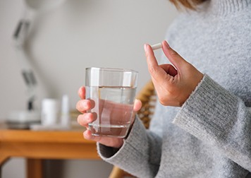 Woman holding glass of water and a pill